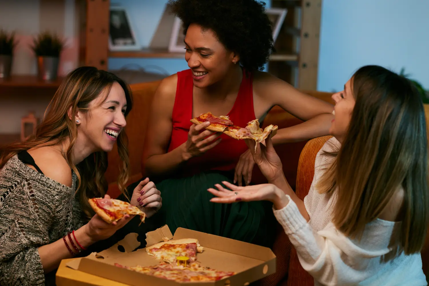 Fröhliche multikulturelle Freundinnen feiern zu Hause und essen Pizza.